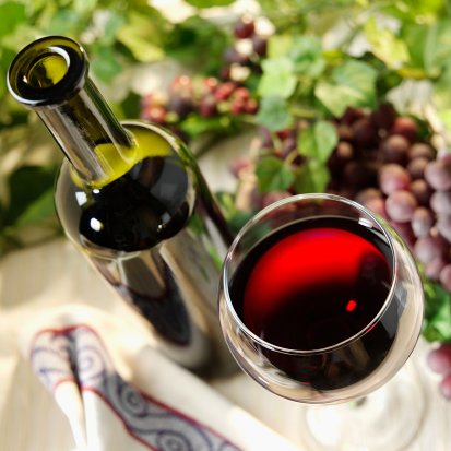 Glass And Bottle Of Red Wine On Table With Napkin, Grape And Grape-Vine (Focus On Bottle And Glass)